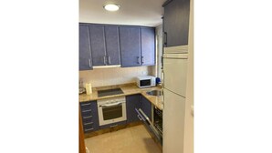 A compact kitchen with dark blue cabinets, a microwave, a dishwasher, and a small oven. - LAUNCHED HOLIDAYS (Sanxenxo)