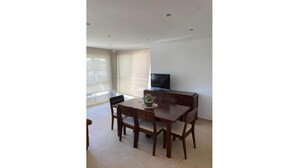 A dining area with a table and chairs, a television on a stand, and a window with blinds. - LAUNCHED HOLIDAYS (Sanxenxo)