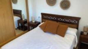 A neatly made bed with a wooden headboard, a bedside table, and a mirror on the wall. - LAUNCHED HOLIDAYS (Sanxenxo)