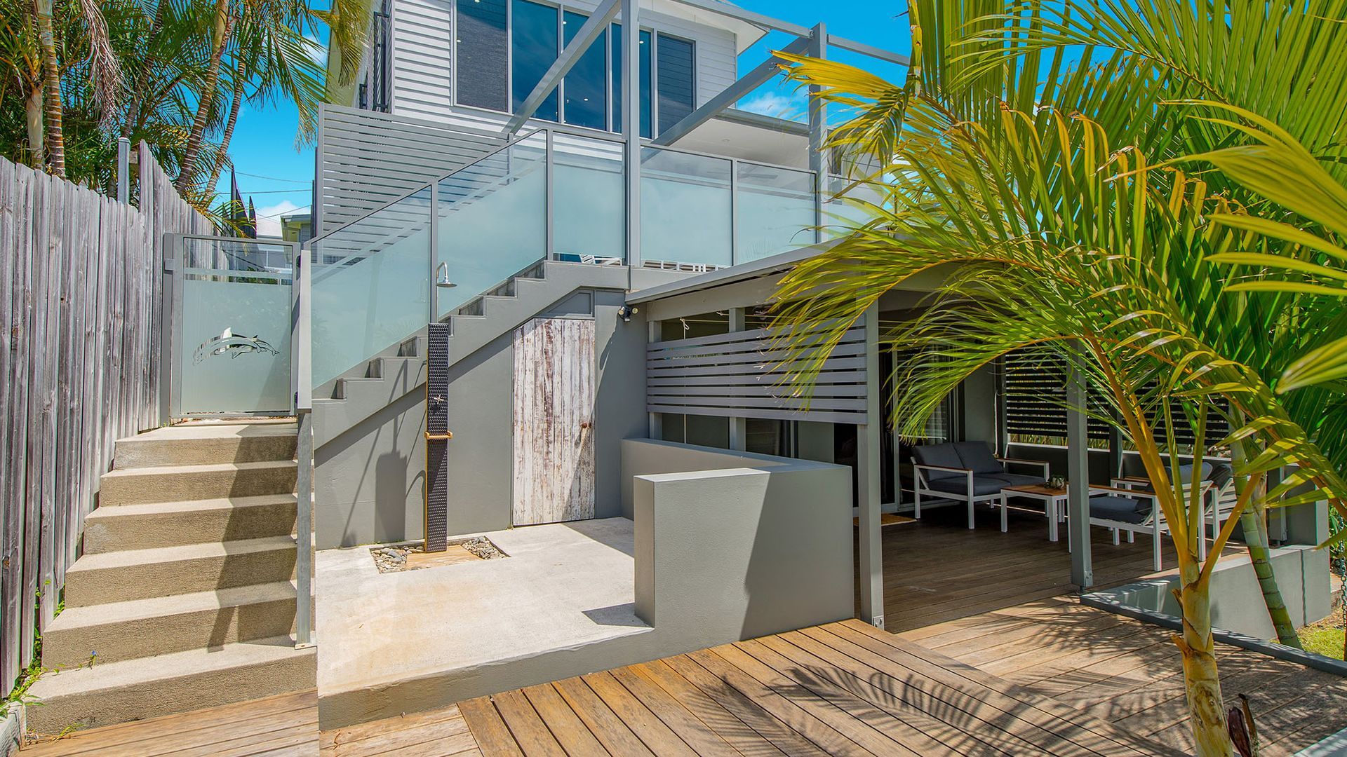 A modern outdoor area with a wooden deck, a staircase, and a seating area with a view of the sky.