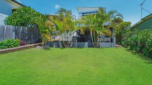 A well-maintained backyard with a lawn, a wooden fence, and various tropical plants.