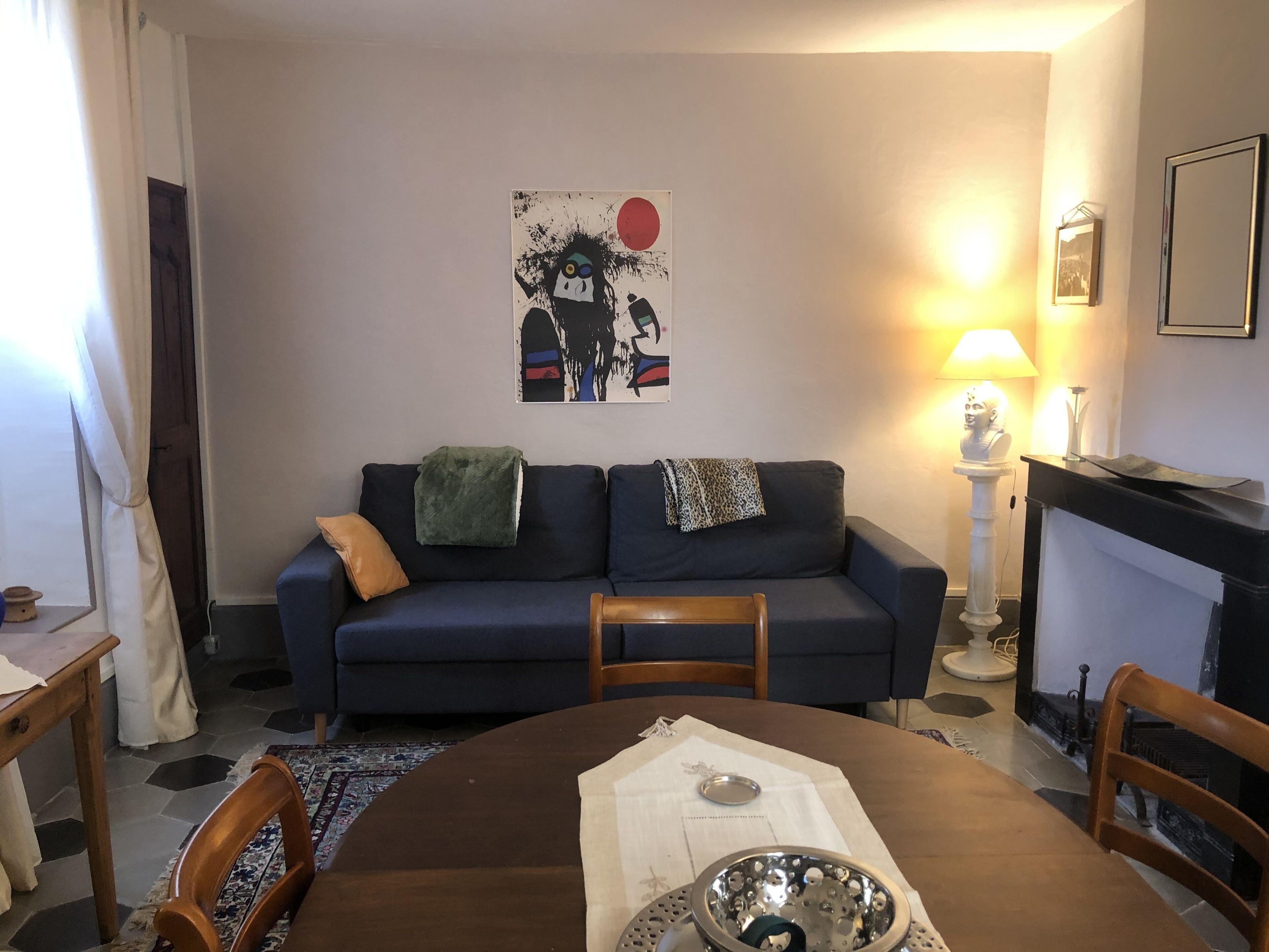 Een woonkamer met een donkerblauwe bank, een ronde houten eettafel en een open haard.