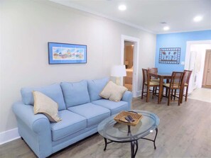 Un salon avec un canapé bleu clair, une table basse en verre et un coin repas avec des chaises en bois.