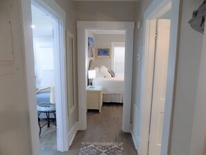A hallway leading to a bedroom with a bed, bedside table, and a chair.
