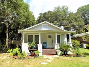 A single-story house with a porch, steps, and potted plants.