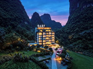 Ein mehrstöckiges Hotel im modernen Stil, umgeben von üppiger Vegetation und Bergen.