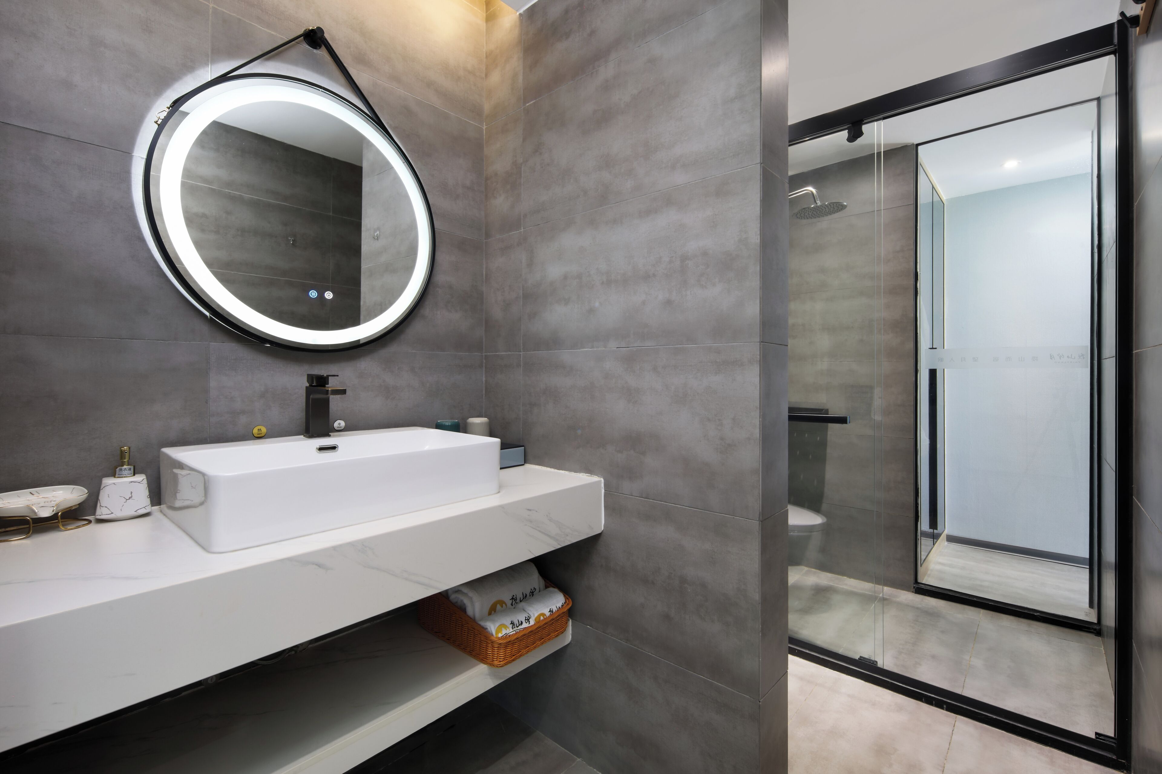 Un baño moderno con un espejo redondo, un lavabo blanco y una ducha con mampara de vidrio.