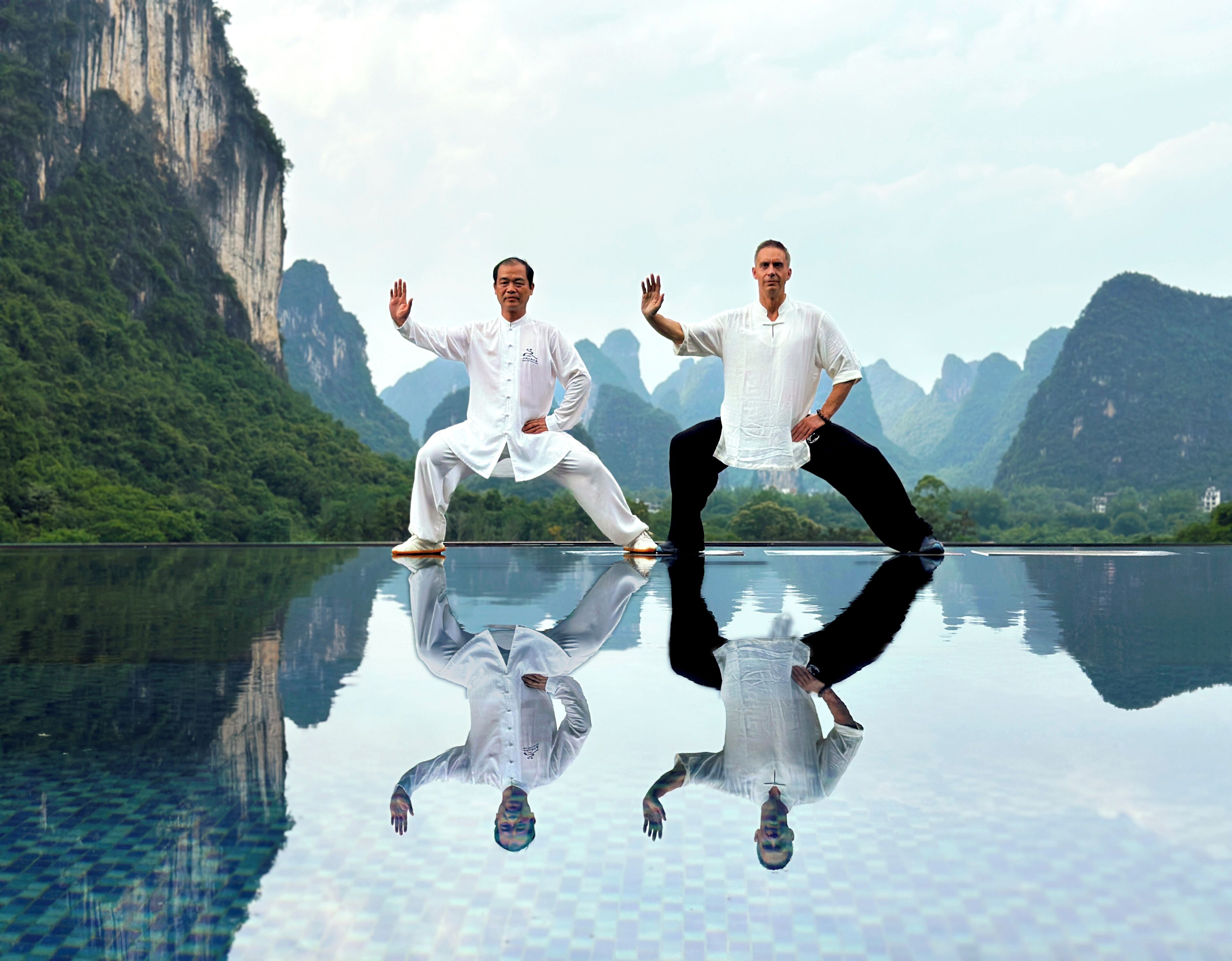 Two individuals in white performing a dance on a reflective surface with a mountainous landscape in the background.
