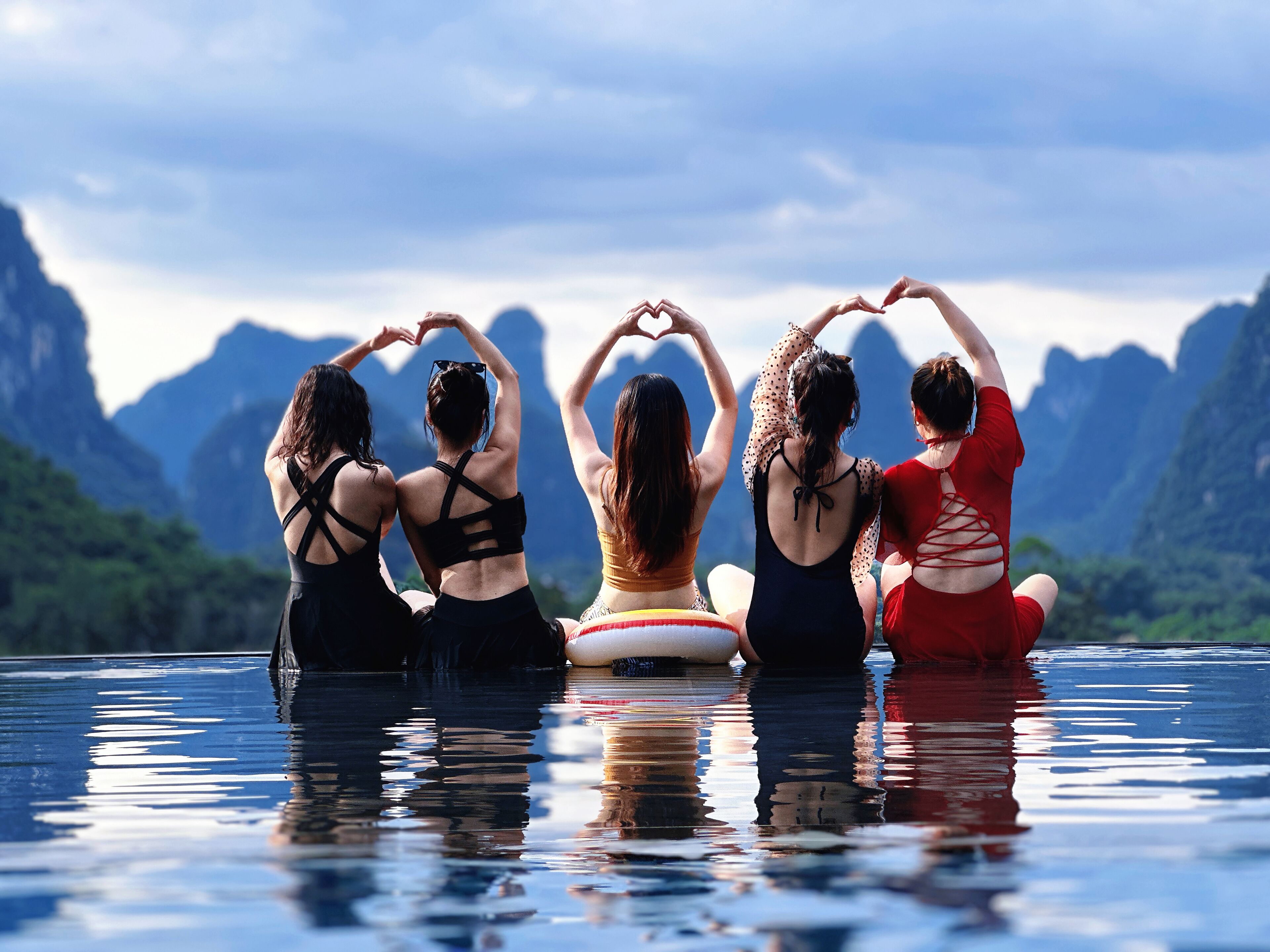 Vier Personen sitzen auf einer schwimmenden Plattform, mit einer gebirgigen Landschaft im Hintergrund.