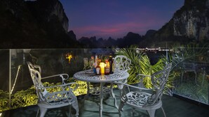 A balcony with a table set for two, surrounded by white metal chairs, overlooking a mountainous landscape at dusk. - Yangshuo Fairyland Hotel (Guilin)
