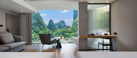 Una habitación moderna con un ventanal grande, un sofá, una silla, una mesita y un escritorio con una planta.