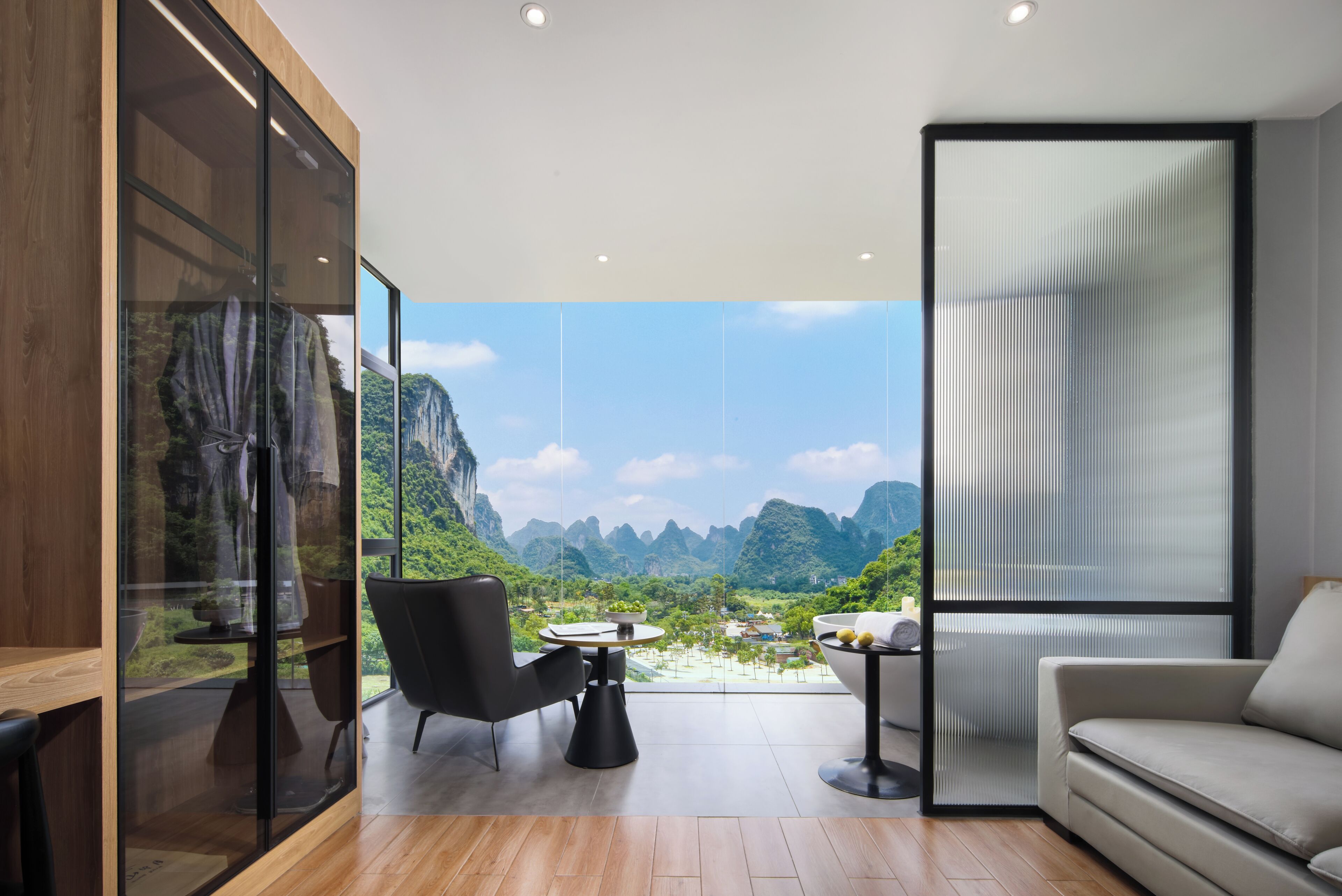 A modern room with a large glass wall, a round table, a sofa, and a chair.