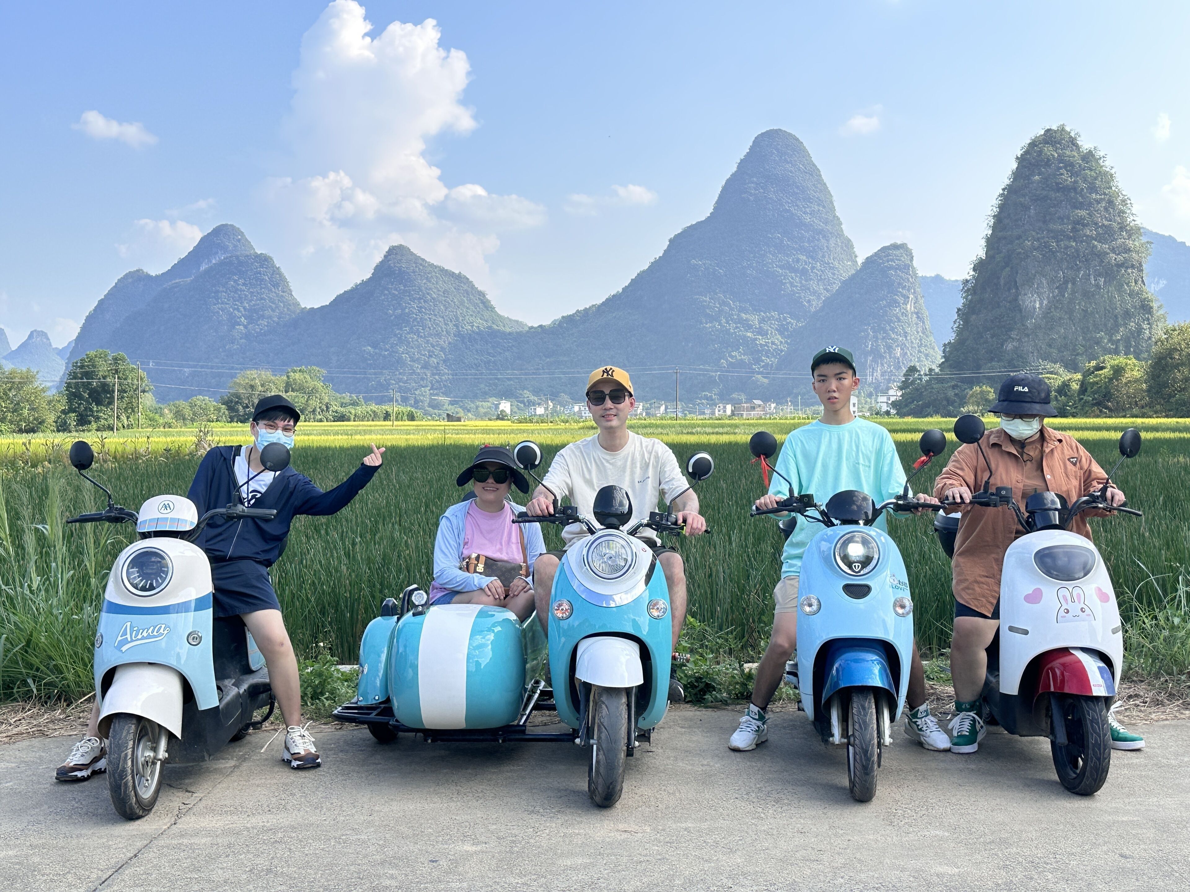 A group of people on scooters in a rural setting with mountains in the background.