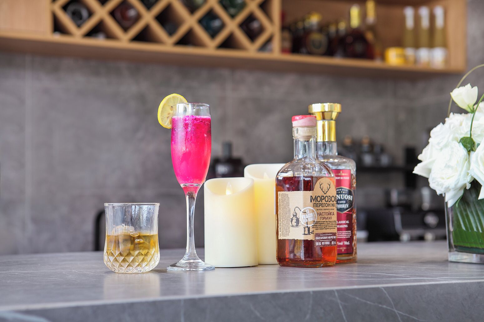 A bar area with a cocktail, a bottle of whiskey, a candle, and a glass.