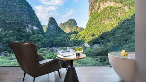Una habitación moderna con vista a un paisaje montañoso, una mesa redonda con un frutero y una bañera blanca.