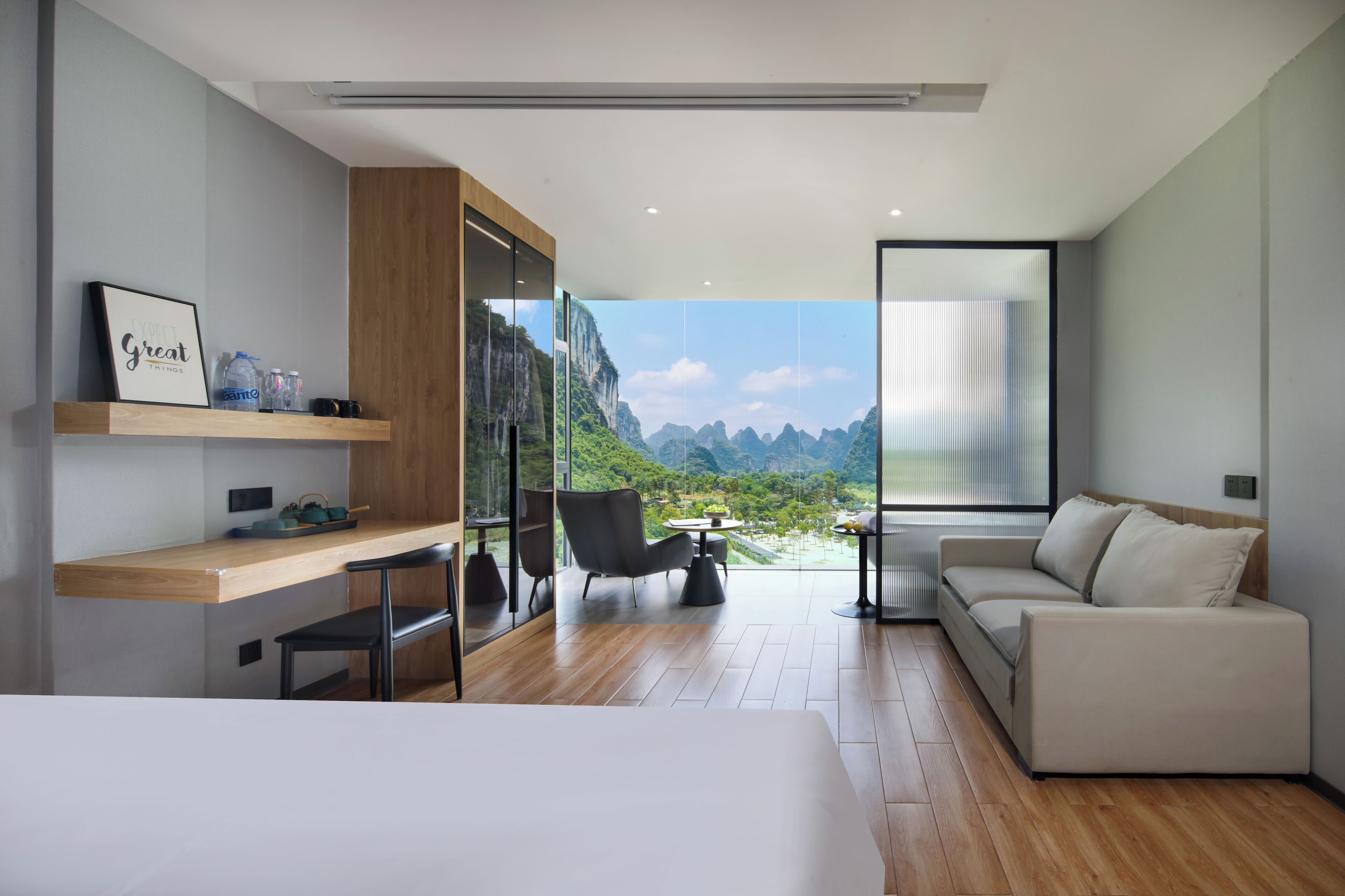 Habitación de hotel moderna con cama, escritorio, silla, sofá y un amplio ventanal con vistas a la montaña.