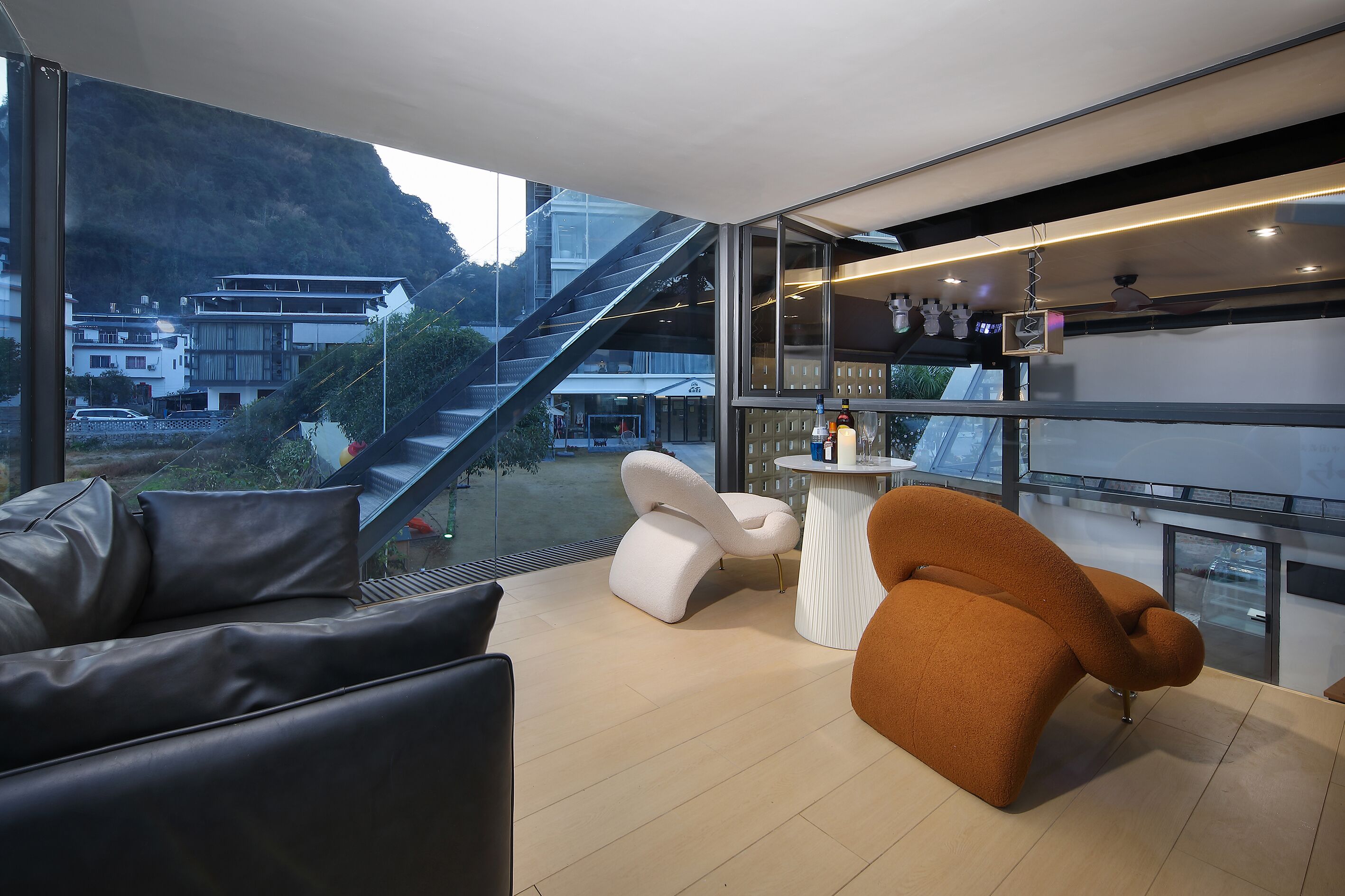A modern interior with a sofa, a white chair, and a table. A staircase is visible outside.