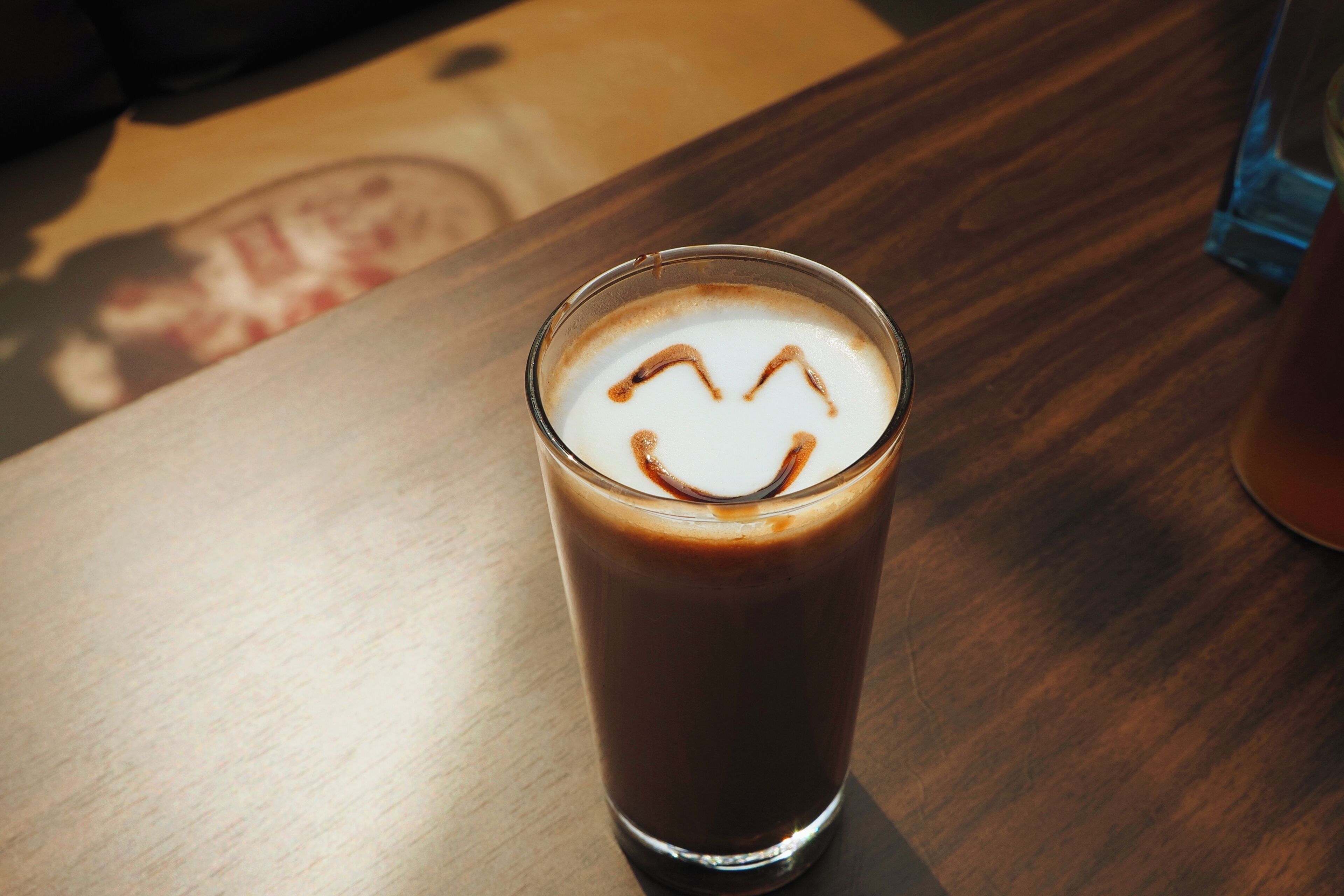 A glass of iced coffee with a smiley face on a wooden table.