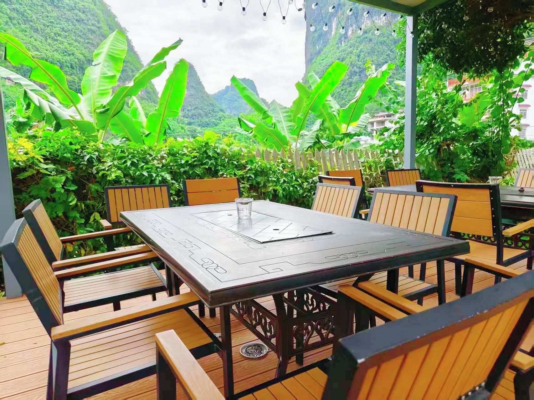 An outdoor patio with a table and chairs, surrounded by lush greenery and mountains in the background.