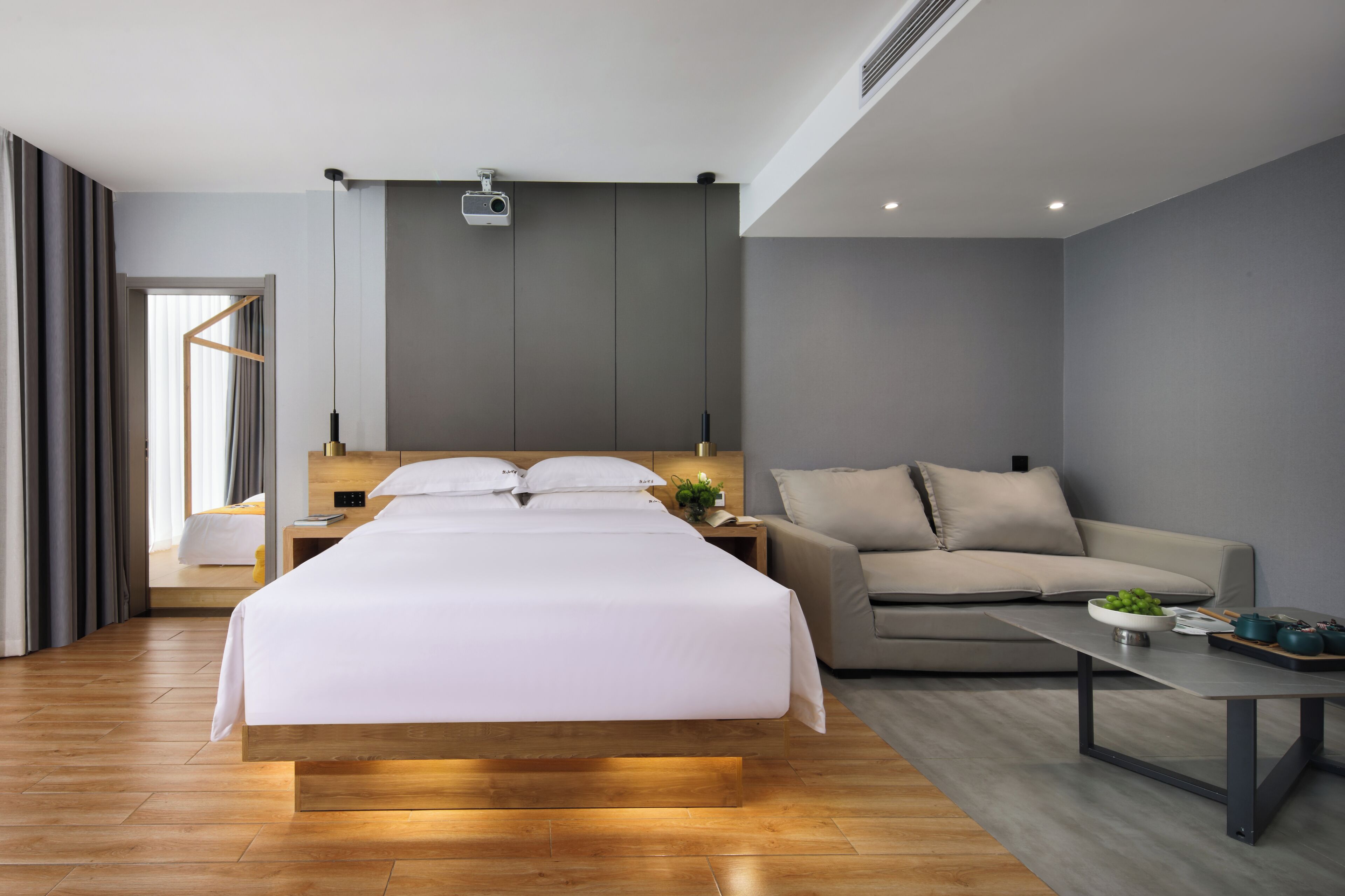 Ein modernes Hotelzimmer mit einem großen Bett, einer Couch, einem kleinen Tisch und einem Projektor an der Decke.