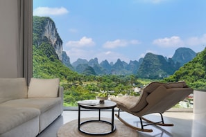 A modern living room with a sofa, a rocking chair, a small table, and a view of a mountainous landscape. - Yangshuo Fairyland Hotel (Guilin)