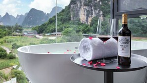 Una bañera con una botella de vino y copas, rodeada de pétalos de rosa, y una vista panorámica de las montañas.