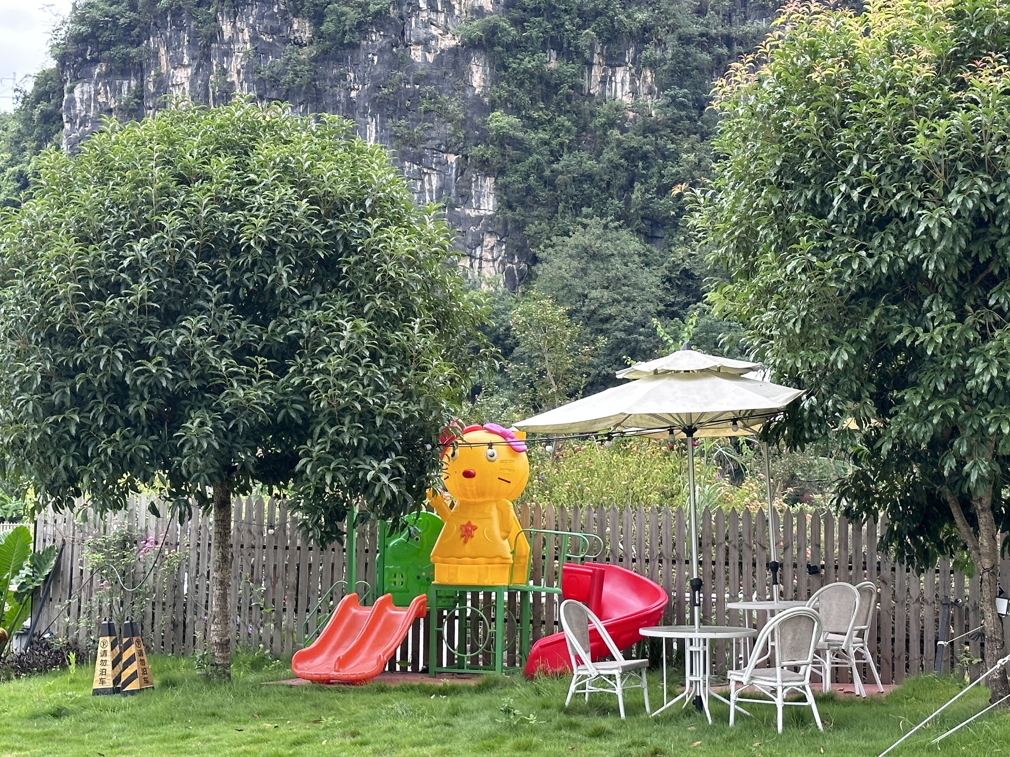 Patio trasero cercado con un tobogán, un juguete inflable amarillo y mobiliario de exterior.