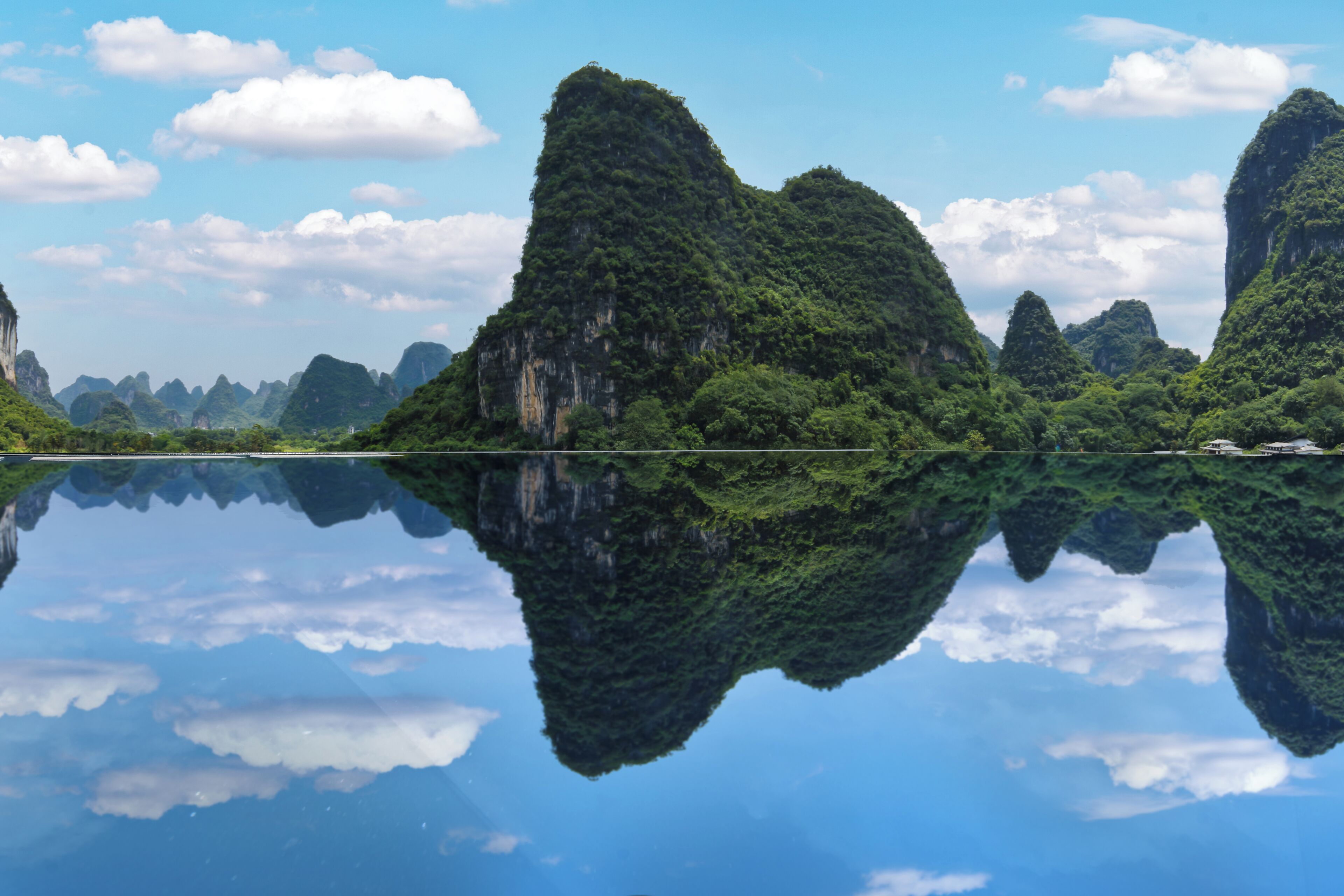 A calm lake with reflections of green mountains and clear blue sky.