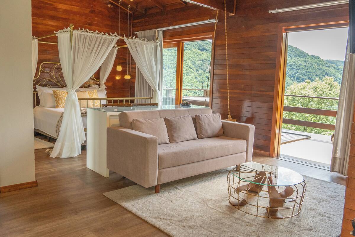 A bedroom with a four-poster bed, a sofa, and a glass table.