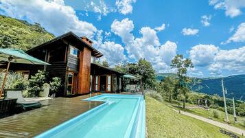 Uma casa moderna com piscina, deck de madeira e vista para as montanhas.