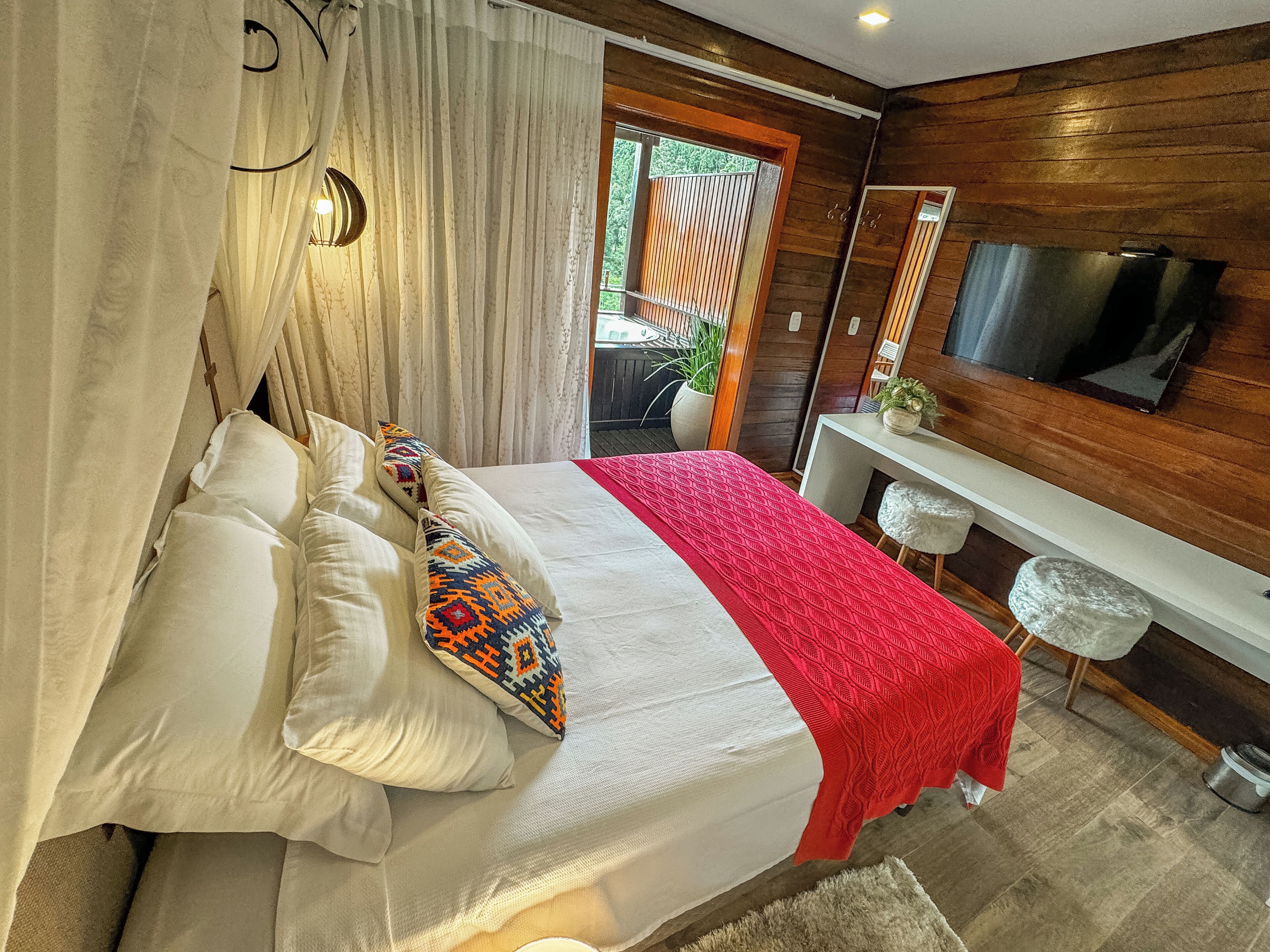 A bedroom with a bed, a TV, a desk, and a window.