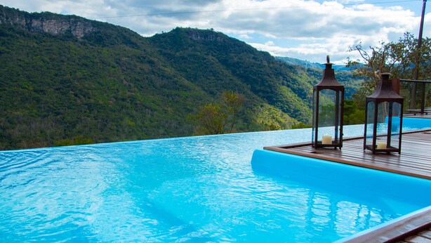 Ein Pool ohne Ende mit einer Holzterrasse, zwei Laternen und Blick auf eine Berglandschaft.