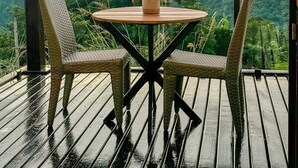 Ein Balkon mit rundem Tisch und zwei Korbstühlen, mit Blick auf eine Berglandschaft im Abendrot.