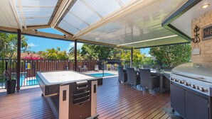 Un espace extérieur abrité comprenant une table de billard, des sièges et un barbecue.