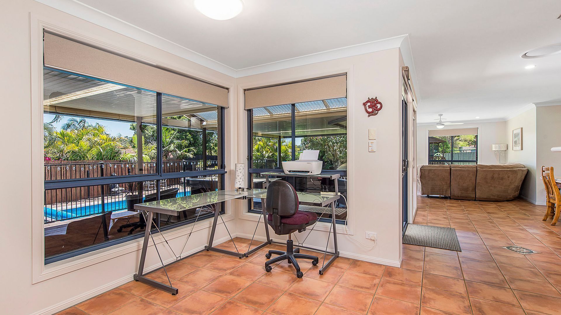 Un despacho en casa con escritorio, silla y grandes ventanales con vistas a una piscina y jardín.
