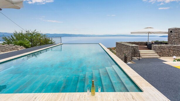 A rectangular pool with a clear blue water surface, a stone wall on one side, and a view of the sea and distant mountains. - Villa Karla, pool with beautiful sea view (Opatija)