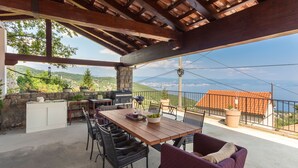 An outdoor patio with a wooden table, chairs, a grill, and a view of the sea. - Villa Karla, pool with beautiful sea view (Opatija)