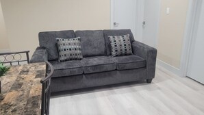Un sofá gris con dos cojines estampados, una mesita redonda con estructura metálica y una puerta blanca al fondo.