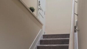 Una escalera alfombrada con barandilla, paredes color crema y una puerta al final.