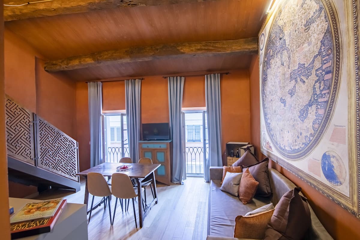 A cozy room with a wooden ceiling, a dining table with chairs, a sofa with cushions, and a large decorative map on the wall.
