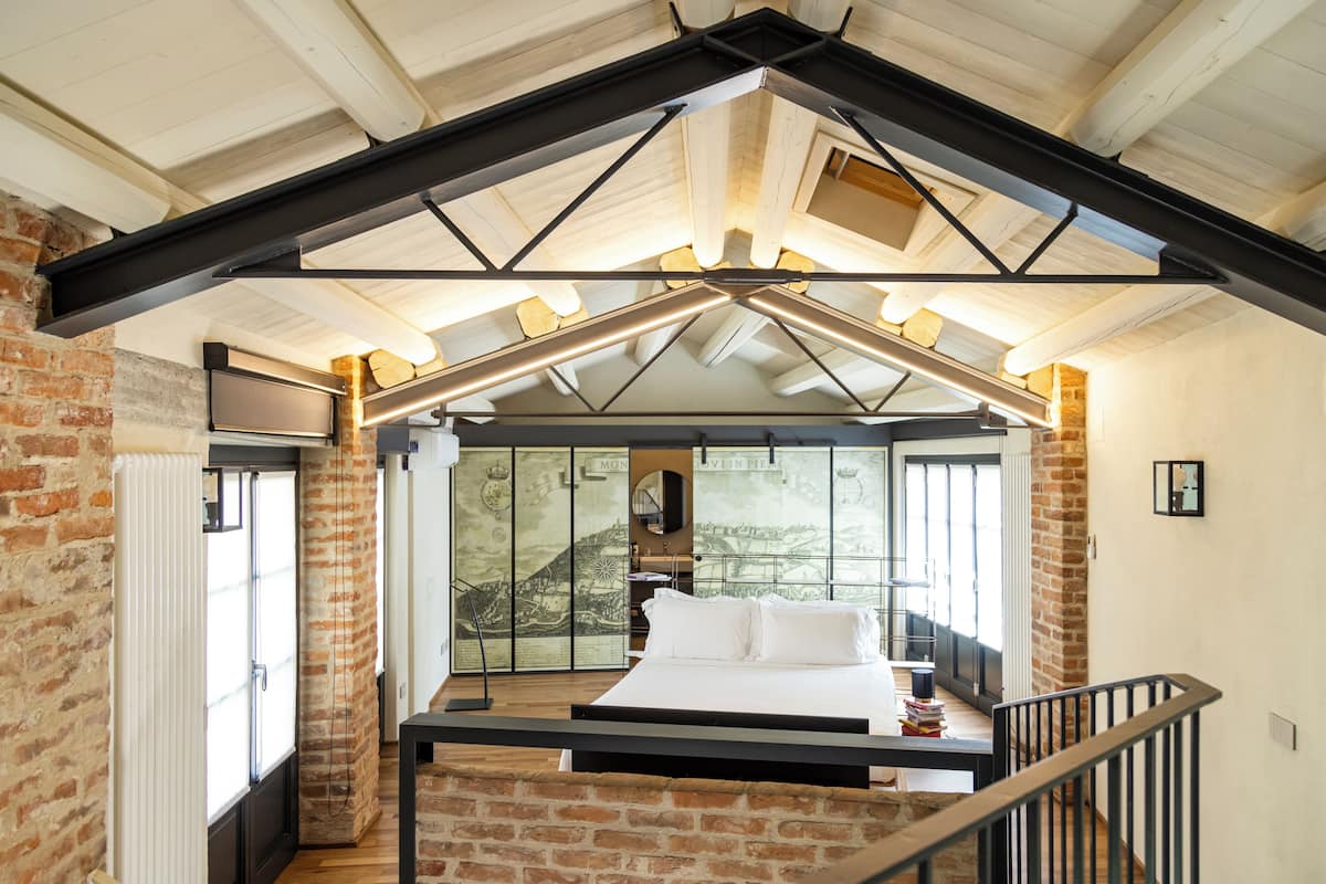 A bedroom with a large bed, a brick wall, and a sloped ceiling with exposed beams.
