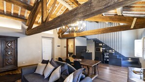 A modern living room with a dark blue sofa, wooden beams, and a chandelier.