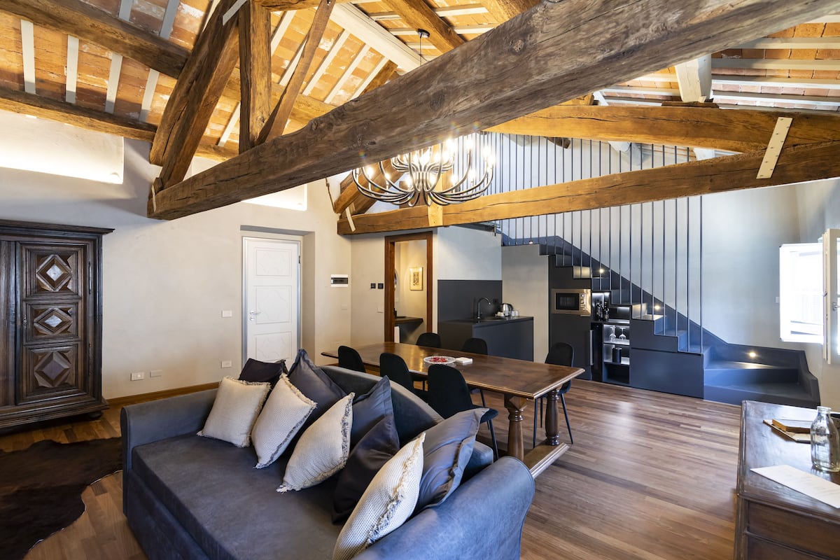 A modern living room with a dark blue sofa, wooden beams, and a chandelier.
