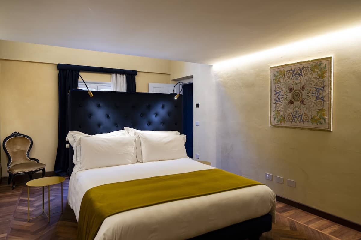 A hotel room with a large bed, a chair, a small table, and a decorative wall piece.