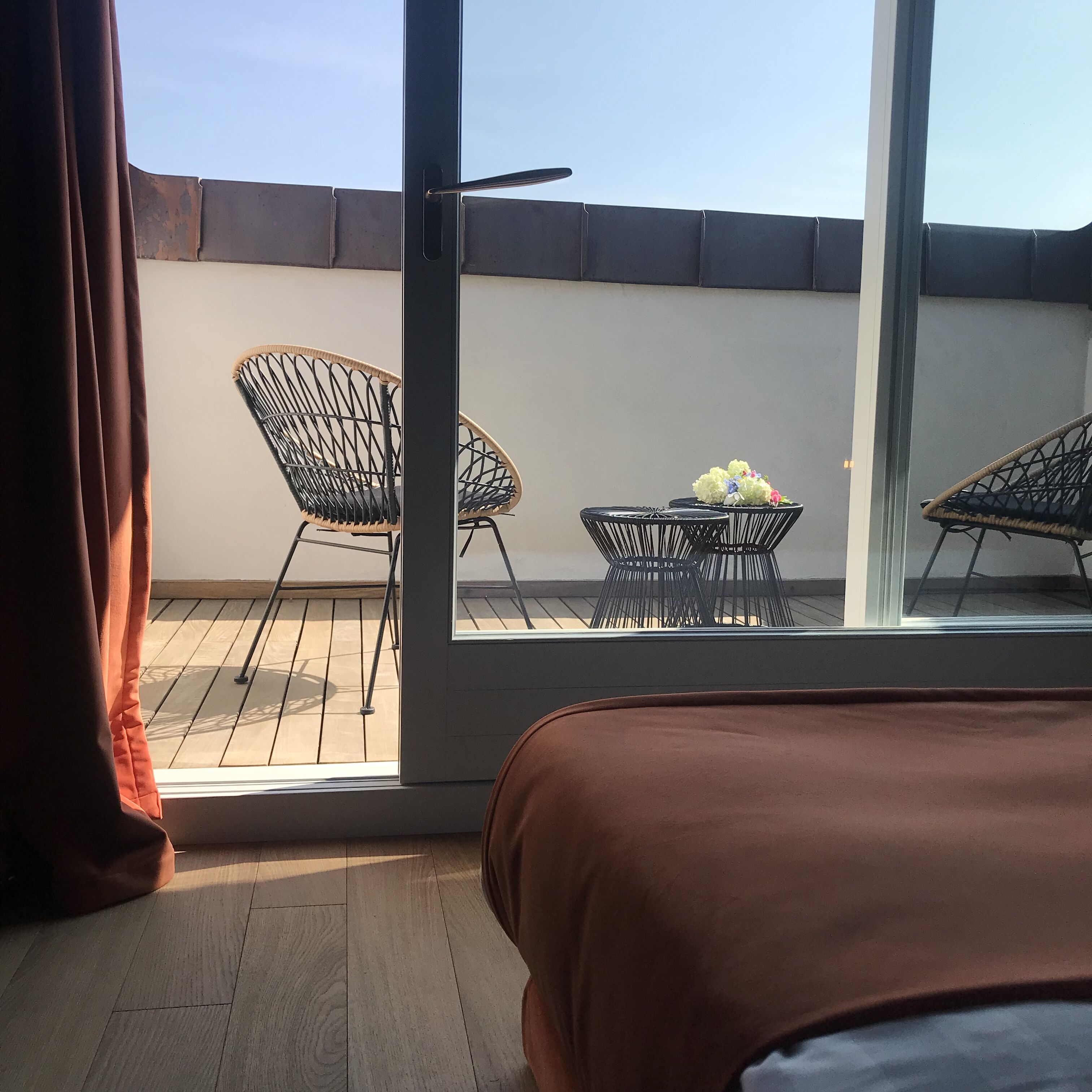 A room with a bed, a window, and a balcony with chairs and a table.