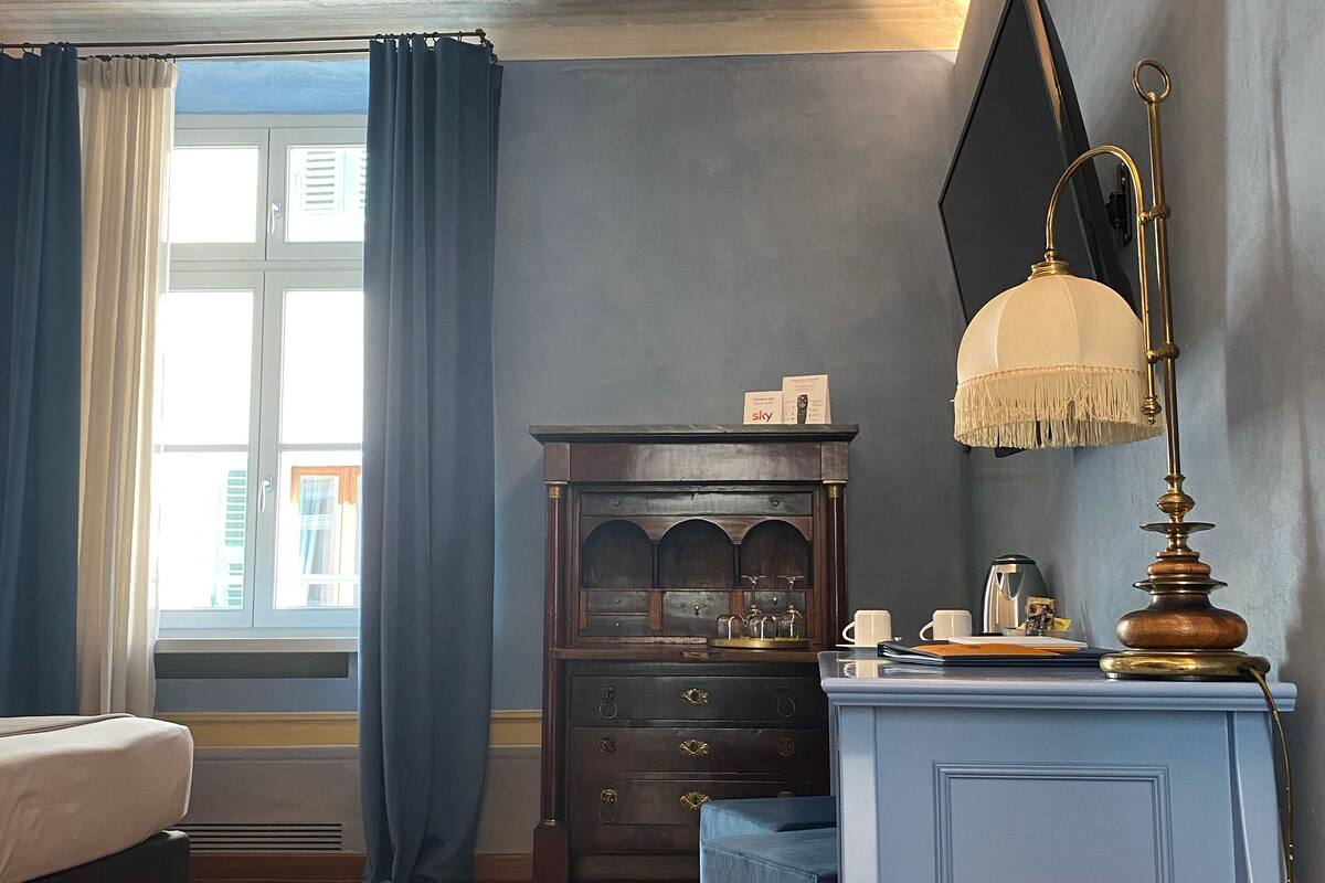A room with a bed, a dresser, a desk with a lamp, and a window with curtains.