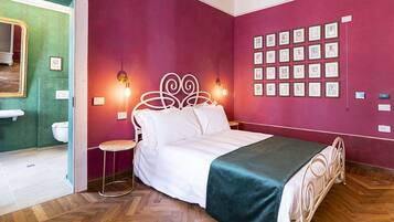 A bedroom with a bed, a stool, a wall with framed pictures, and a mirror.