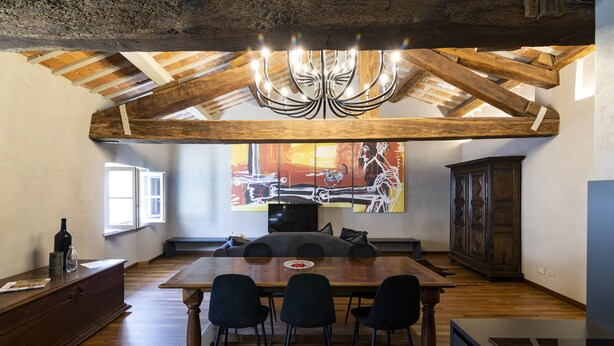 A dining area with a wooden ceiling, a chandelier, a large painting, and a dining table with chairs. - Palazzo Fauzone Relais (Mondovi)