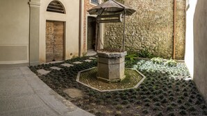 A courtyard with a stone fountain, a wooden door, and a stone wall with a metal railing. - Palazzo Fauzone Relais (Mondovi)