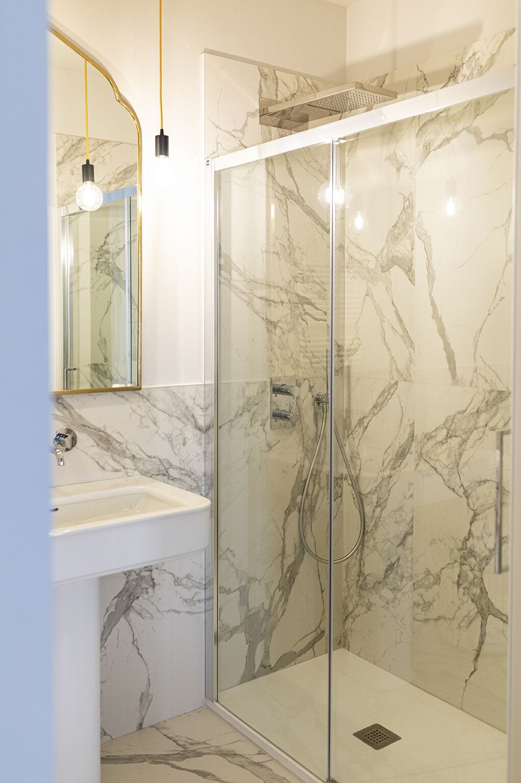 Un bagno moderno con doccia vetro, pareti in marmo e lavandino bianco.